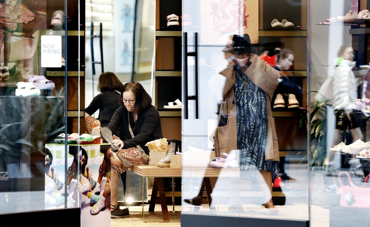 Shoppers, some with masks and some without, try on shoes in a mall