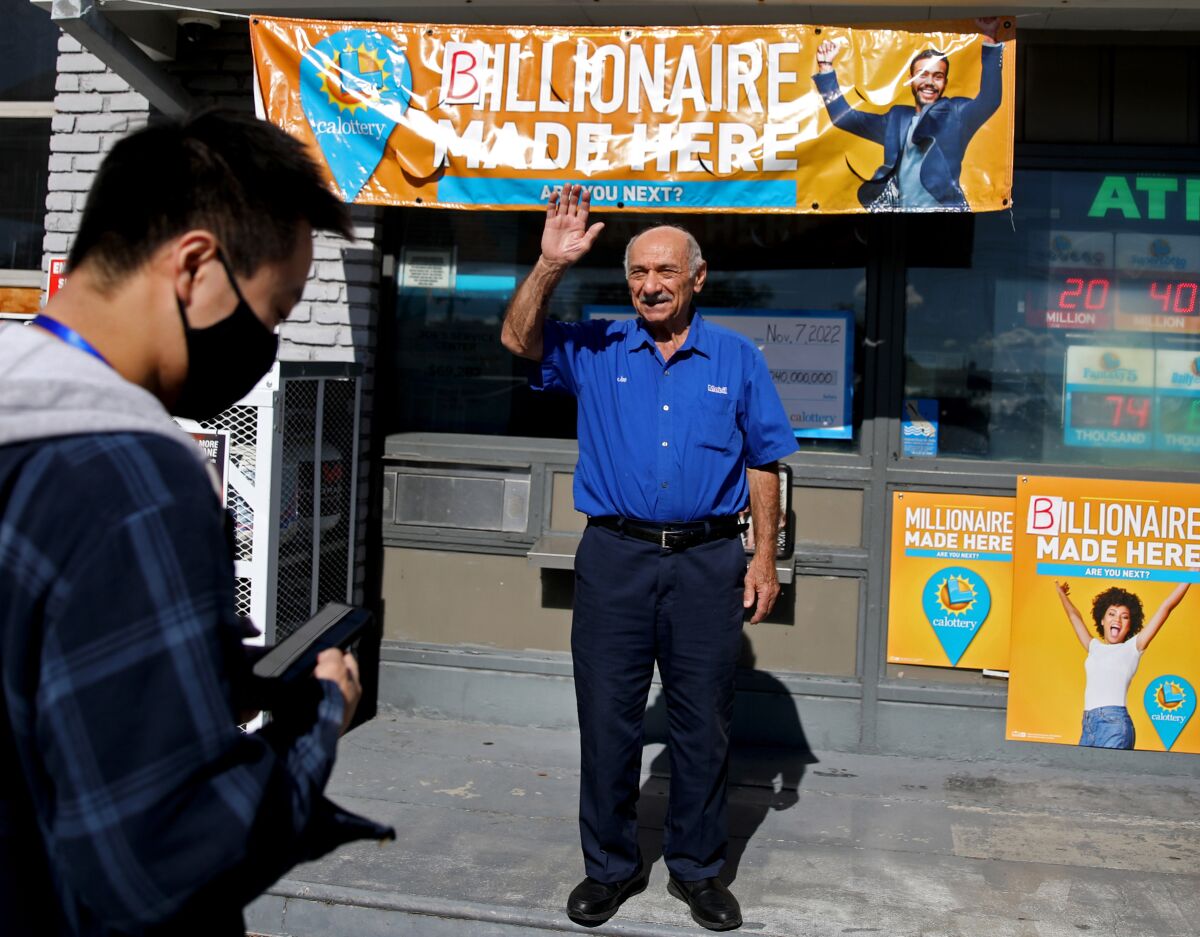A man waves outside a gas station with a California Lottery banner that says "Billionaire made here"