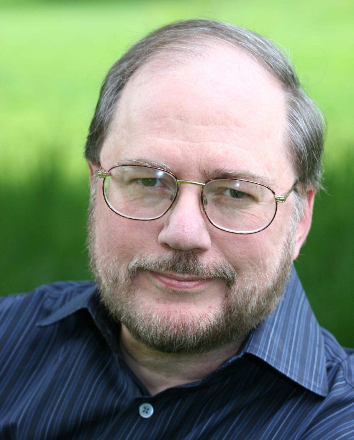 A close-up portrait of a bearded man with glasses