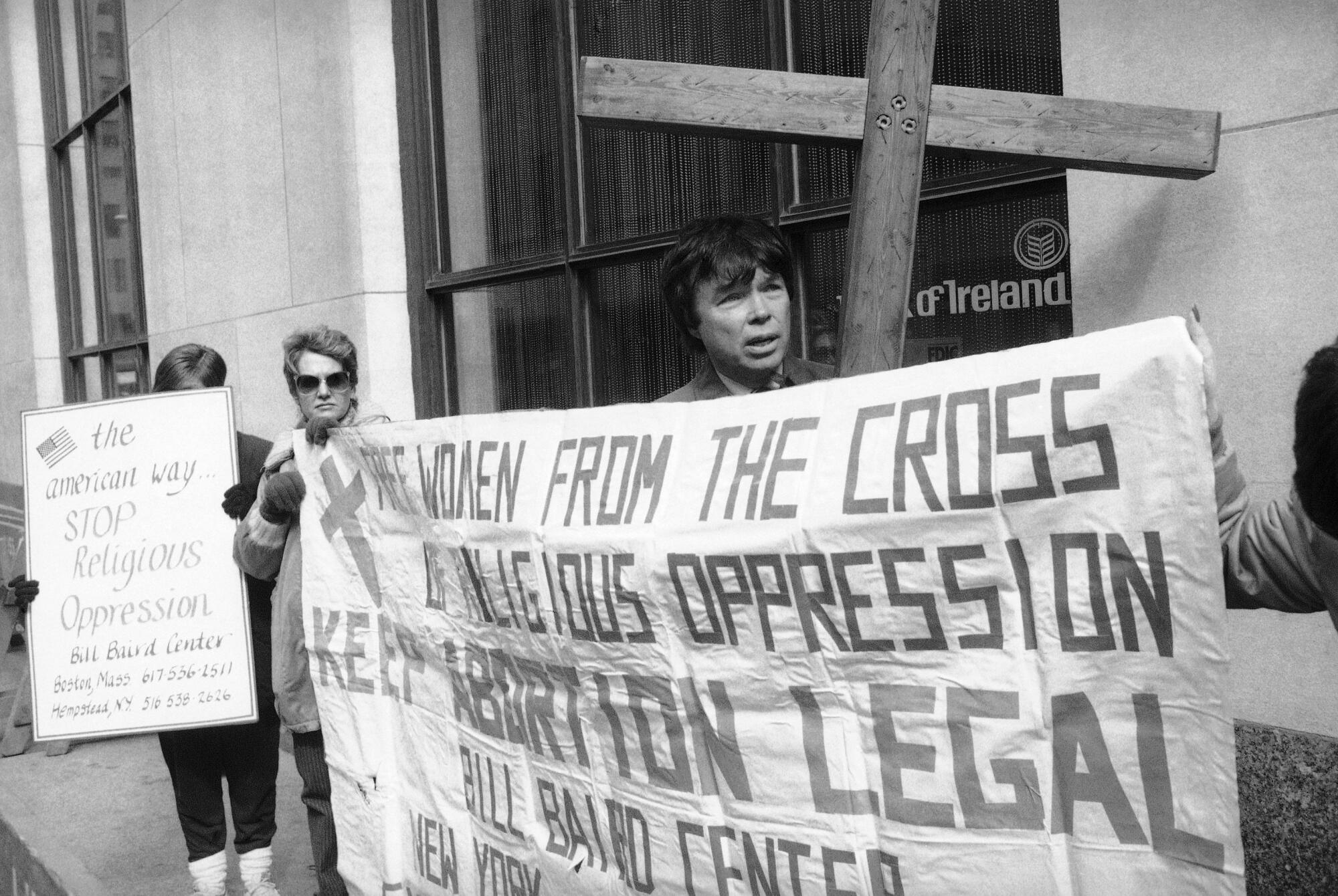 A man holds a big wooden cross and a banner.
