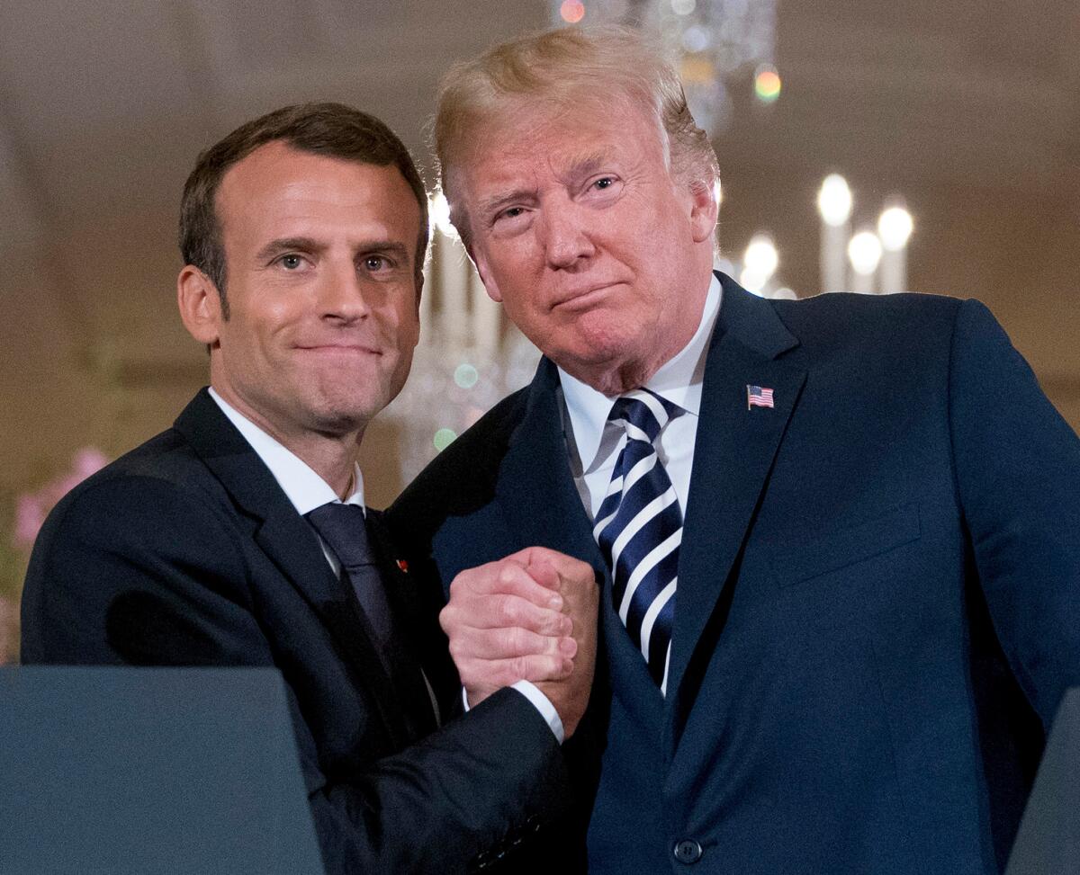 Presidents Emmanuel Macron of France, left, and Donald Trump stand side by side, hands clasped.
