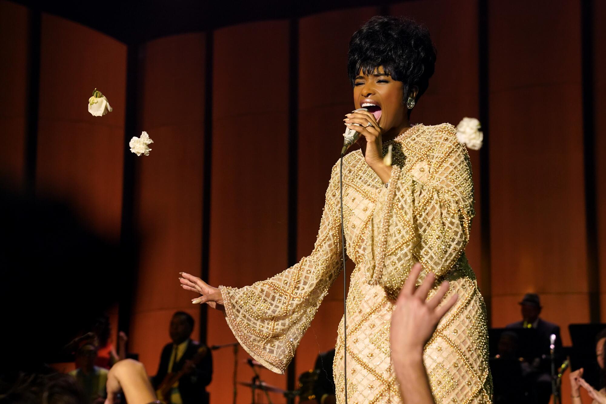 A woman in a white and brown dress sing into a microphone 