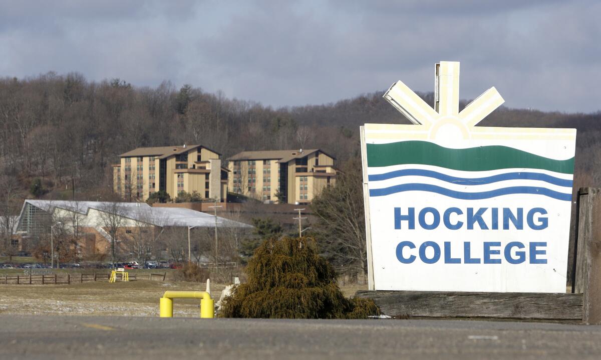 A sign reads "Hocking College." Apartment buildings and a forested hill are on the horizon.