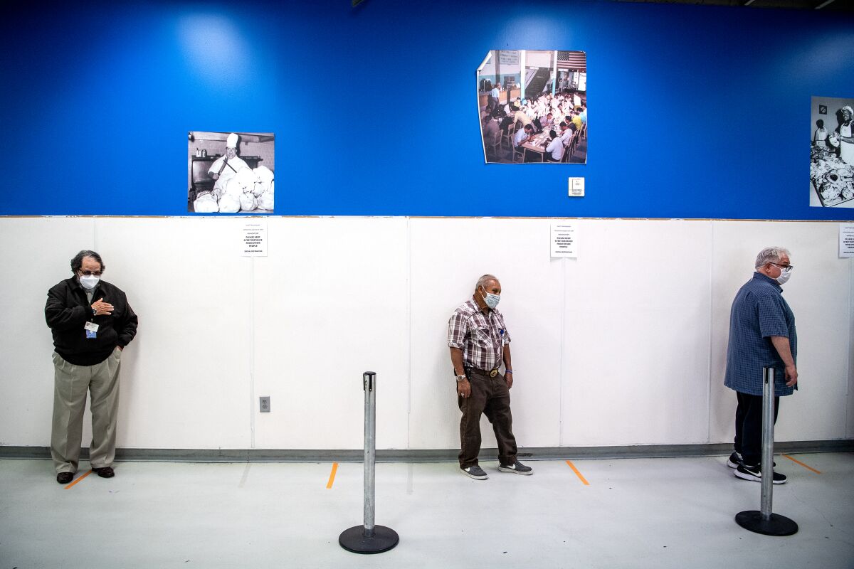 Three men line up six feet apart at Union Rescue Mission in downtown Los Angeles. 