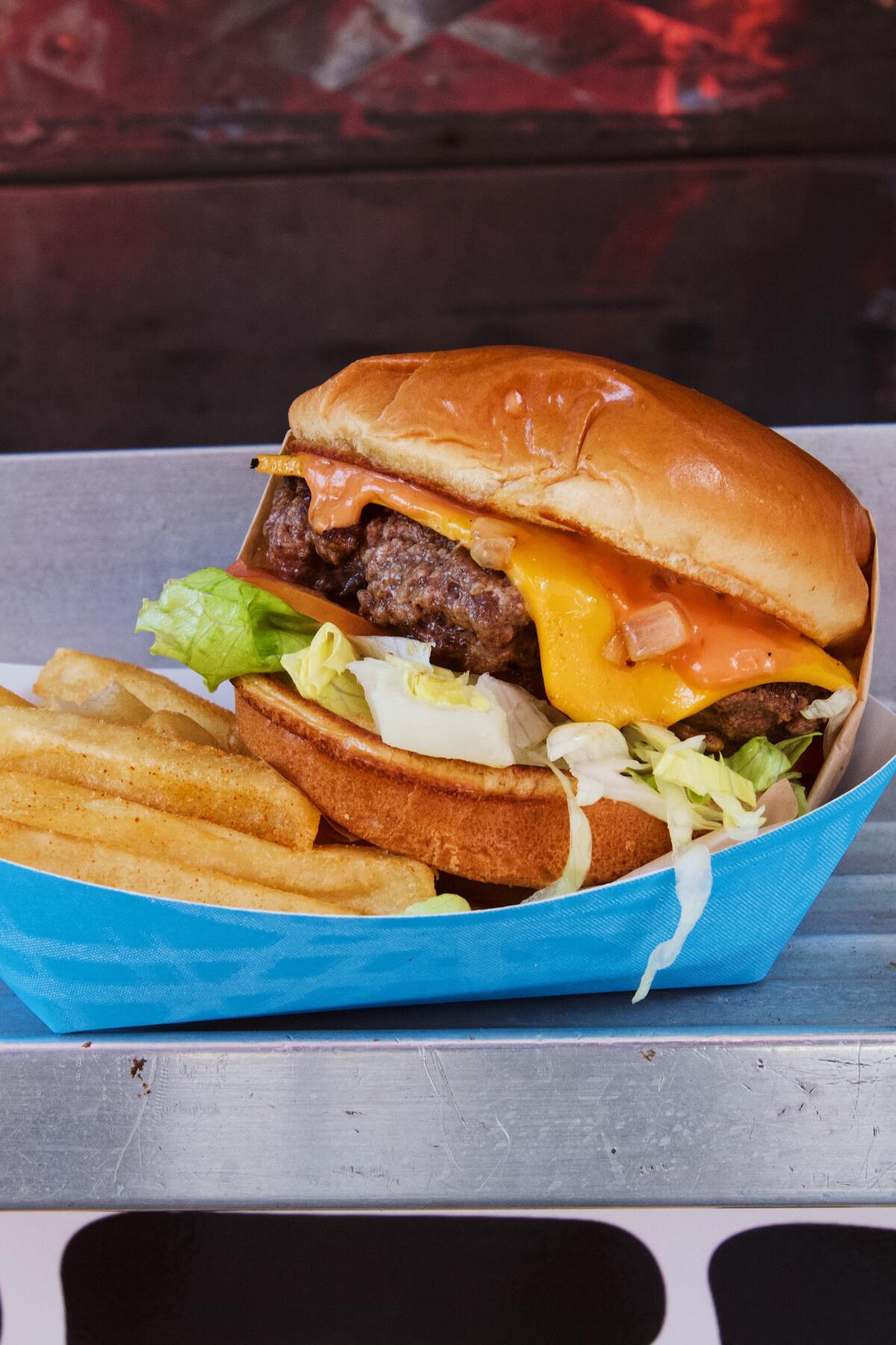 A single Thicc Burger cheeseburger with fries in a blue cardboard dish.