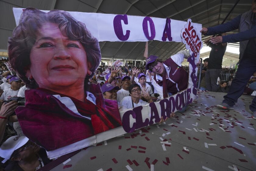 Delfina Gómez, candidata del partido Morena a la gubernatura del Estado de México, a la derecha, posa junto a una pancarta con su imagen durante un evento de campaña, el domingo 28 de mayo de 2023, en el Valle de Chalco, México. (AP Foto/Marco Ugarte)