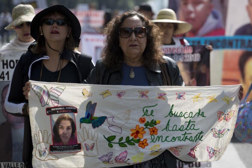 A woman holds a blanket embroidered with a message that reads in Spanish: "I will look for you until I find you", and adorned with an image of a disappeared youth during a march on Mother's Day in Mexico City, Thursday, May 10, 2018. Mothers and other relatives of persons gone missing in the fight against drug cartels and organized crime are demanding that authorities locate their loved ones. (AP Photo/Eduardo Verdugo)