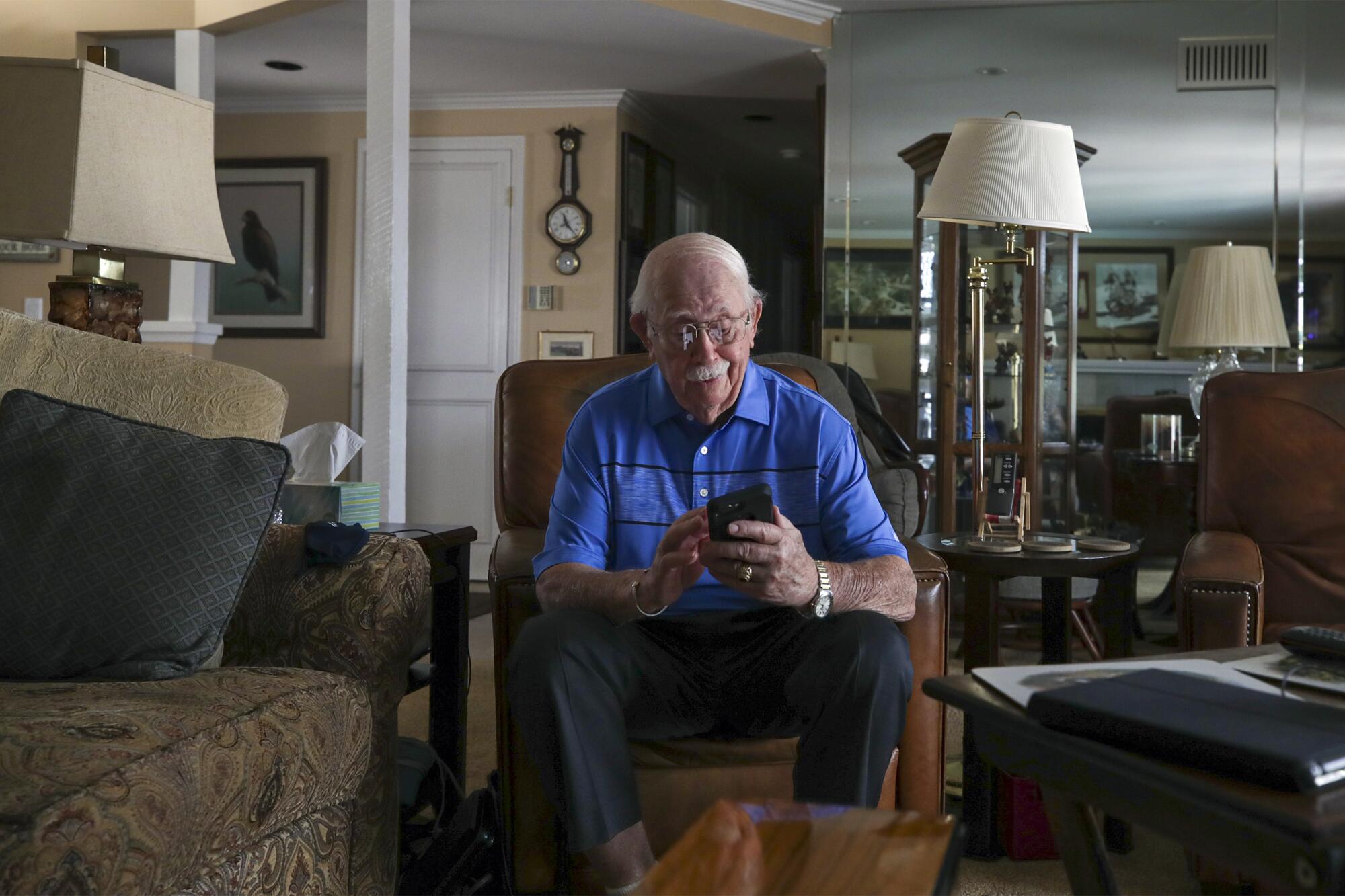 A man sits in a chair at home looking at his phone