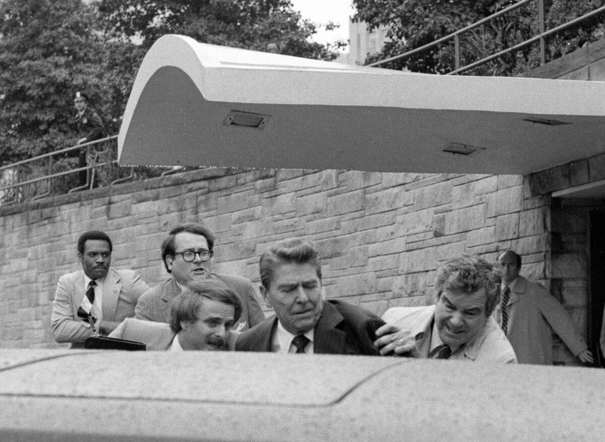 ARCHIVO - El presidente Ronald Reagan es empujado hacia su limusina por agentes del Servicio 