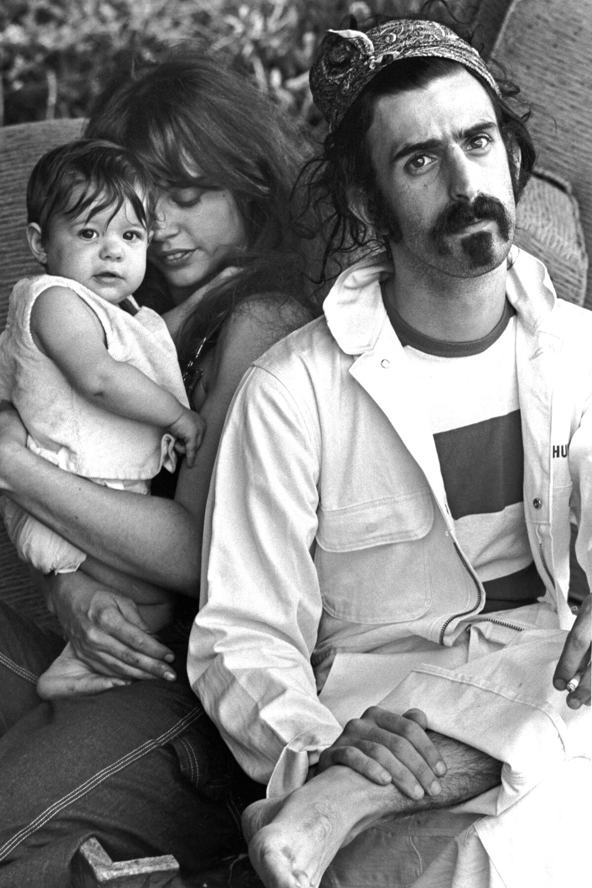 A black-and-white photo of Frank Zappa with Gail Zappa holding newborn Moon Unit Zappa.