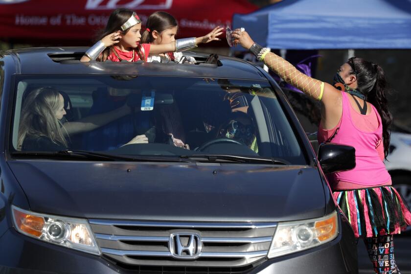 MONTEREY PARK, CA - OCTOBER 29: Jennifer Olivas of Monterey Highlands PTA hands treats to six-year-old twins Loucia (cq) Ramirez, left, and Adriana Ramirez during the Monterey Park Candy Caravan on Thursday, Oct. 29, 2020 at Highlands Park. The drive-through trick-or-treat was held at five locations around the city. (Myung J. Chun / Los Angeles Times)