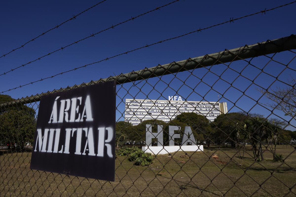 A sign on a fence that's topped with barbed wire reads "Area Militar." A building behind the fence says "HFA."
