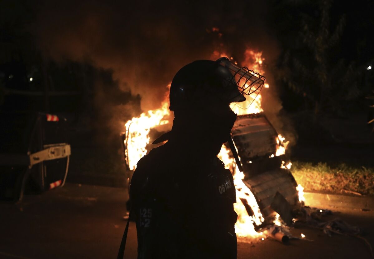 A police officer in riot gear stands behind a burning barricade during protests against the death of a man who was detained by police for violating social distancing rules to curb the spread of the new coronavirus, in Bogota, Colombia, Thursday, Sept. 10, 2020. Javier Ordonez died in a hospital Wednesday after receiving repeated electric shocks with a stun gun from officers who detained him, seen on a video taken by Ordonez's friend, and published on social media. (AP Photo/Fernando Vergara)