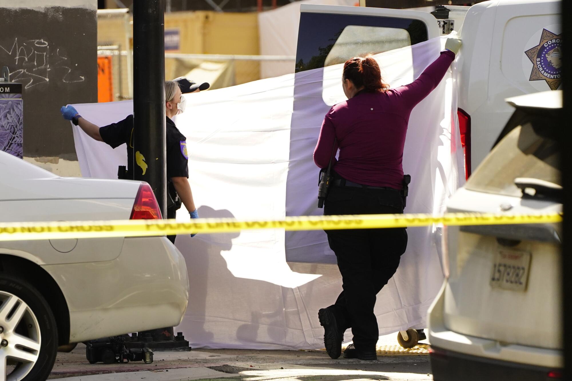 A sheet is held up to block from view the transfer the body of a victim into a coroner's van