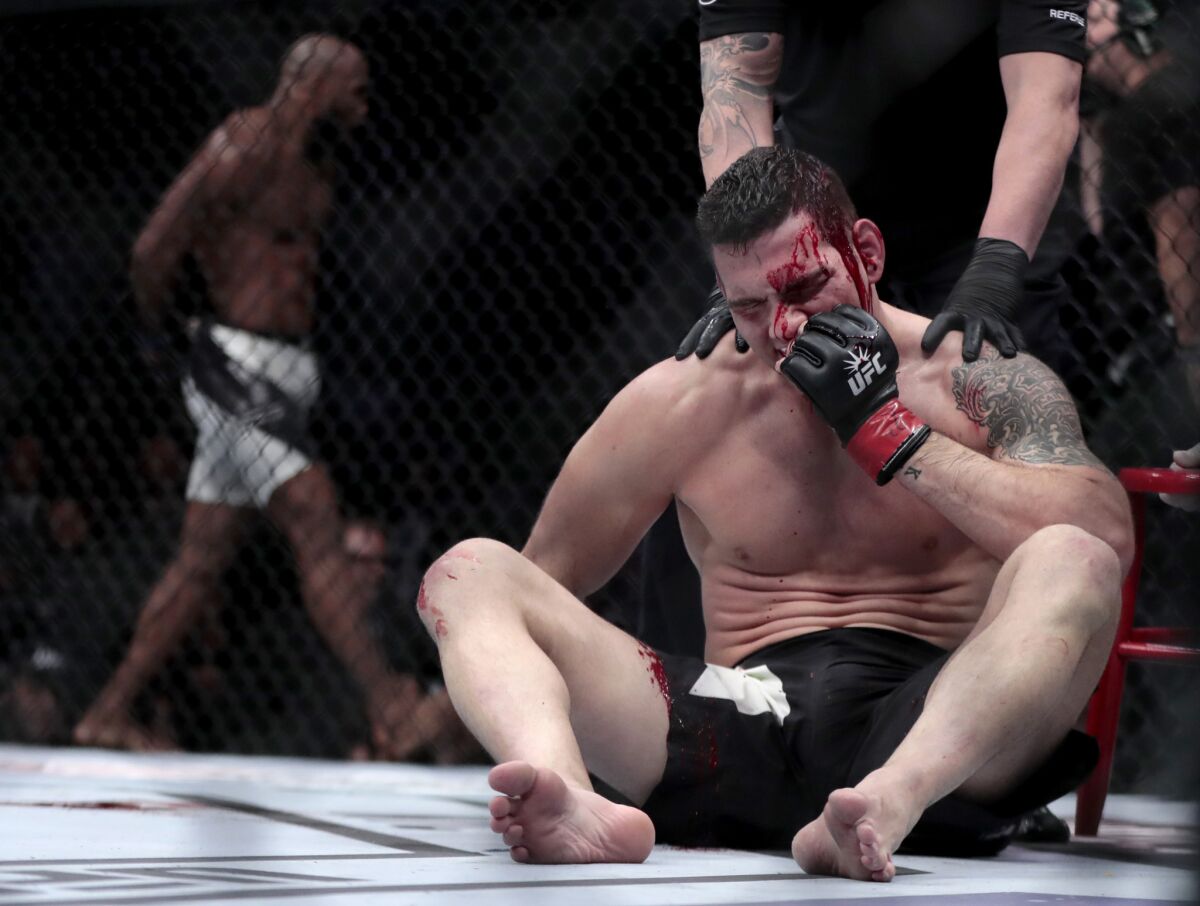 Chris Weidman sits in the octagon after being knocked out by Yoel Romero, background, during a middleweight fight at UFC 205.