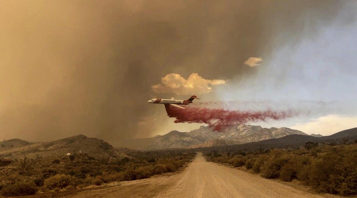 An air tanker drops fire retardant over a road surrounded by greenery.