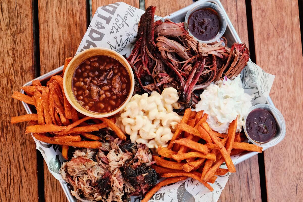 A tray of shredded brisket, pulled pork, brisket baked beans, coleslaw, sweet potato fries and mac and cheese on a wood table