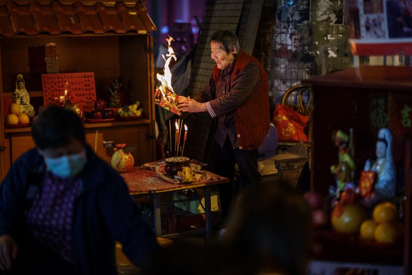 HONG KONG, HONG KONG SAR -- THURSDAY, MARCH 12, 2020: Grandma Leung burns a spell and waves it around to ward off bad luck as she prepares to do a ceremony called 'villain hitting,' in the Causeway Bay district of Hong Kong, China, on March 12, 2020. Villain hitting, or locally known as "Da siu yan" in Cantonese which translates to "hitting away petty little people" derives from religious practice originating from Guangdong Province. The idea is akin to demon exorcising, or cursing one's enemy, by beating a paper effigy of them with a slipper or shoe against a brick and casting spells. (Marcus Yam / Los Angeles Times)