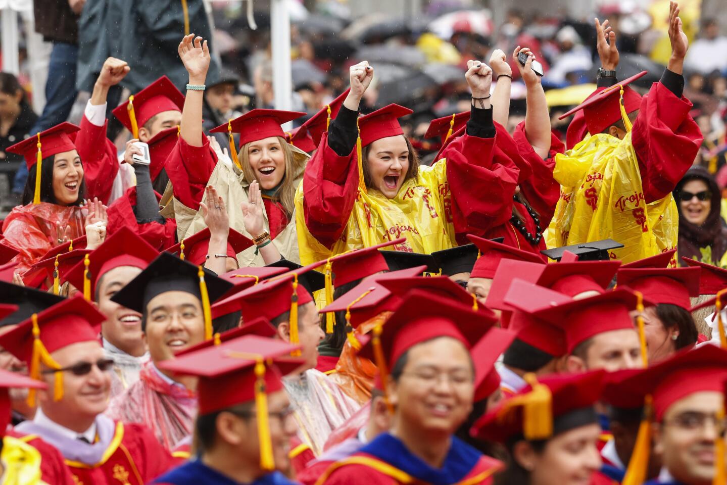 USC graduates wear ponchos over their caps and gowns while cheering in the rain during commencement ceremonies.