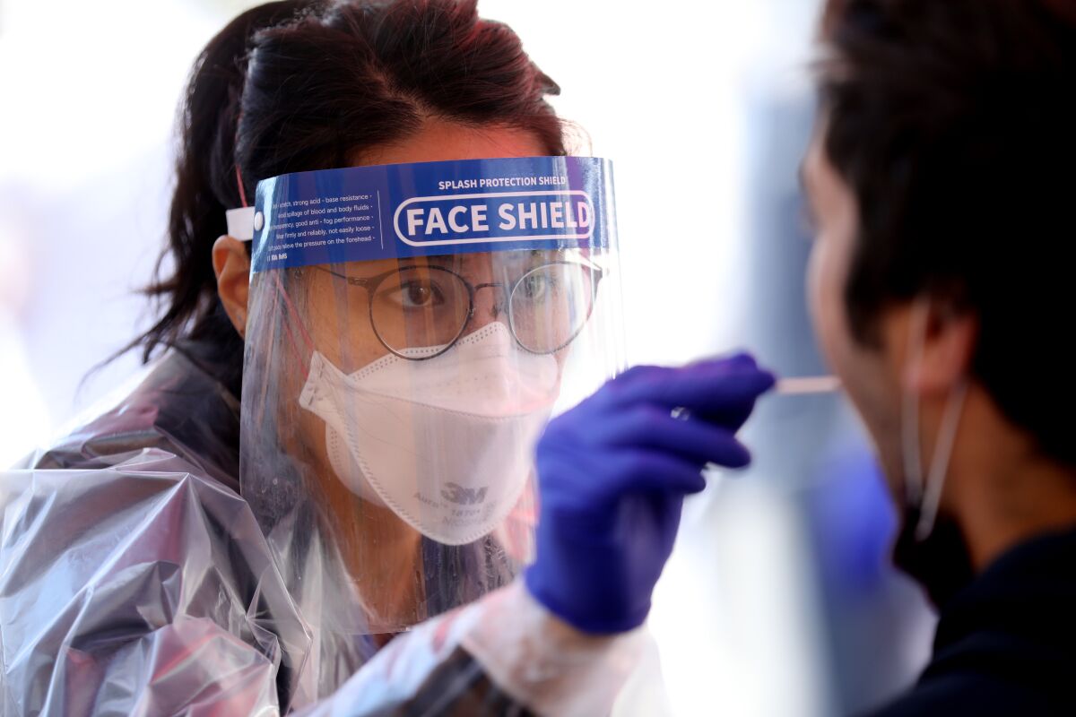 Nursing student Kathryn Domingo, in face mask and shield, gives a COVID-19 test to a person.