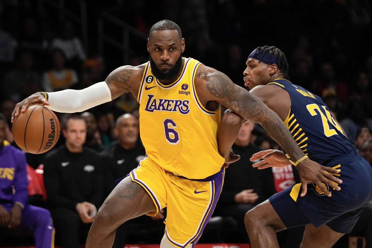 El jugador de Los Lakers de Los Ángeles LeBron James, a la izquierda, avanza junto al jugador de los Pacers