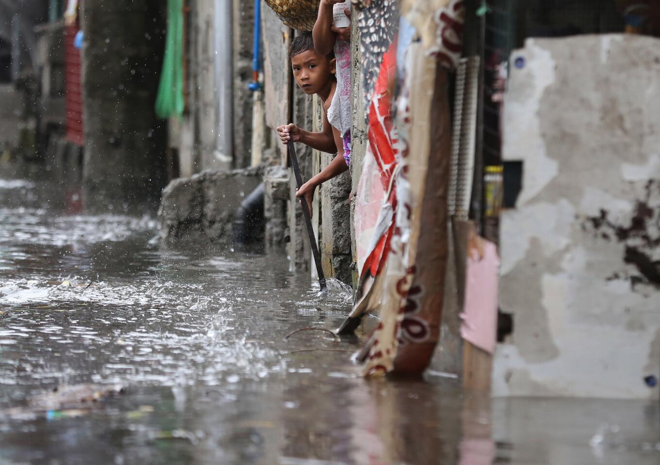 A boy tries to sweep out floating debris from his flooded home as Typhoon Rammasun batters suburban Quezon city, north of Manila.