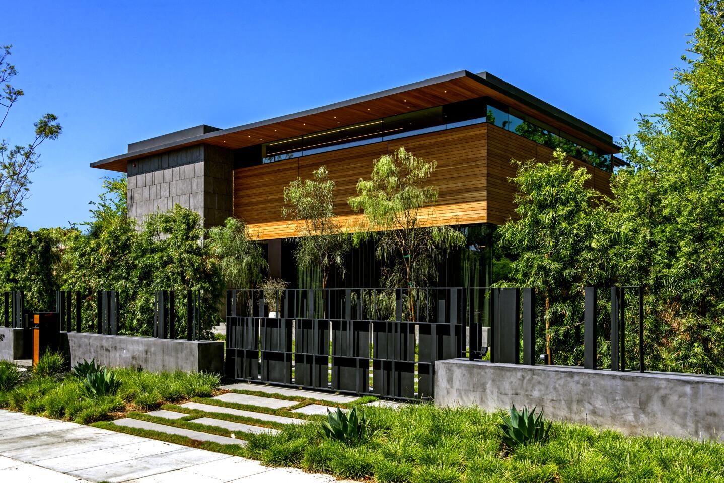 The 11,438-square-foot home, designed by Tag Front Architects, is visually striking from the street with its wood siding, stone accents and thin bands of clerestory windows. Walls of glass open the common areas to an infinity-edge swimming pool and spa. A detached guest house also lies in the backyard. Listed for $17.995 million, the modern residence has six bedrooms and 8.5 bathrooms including a master suite with an artistic fireplace feature. A floor-to-standing fireplace divides dual living rooms that make up the common area. A designer-done kitchen sits nearby.