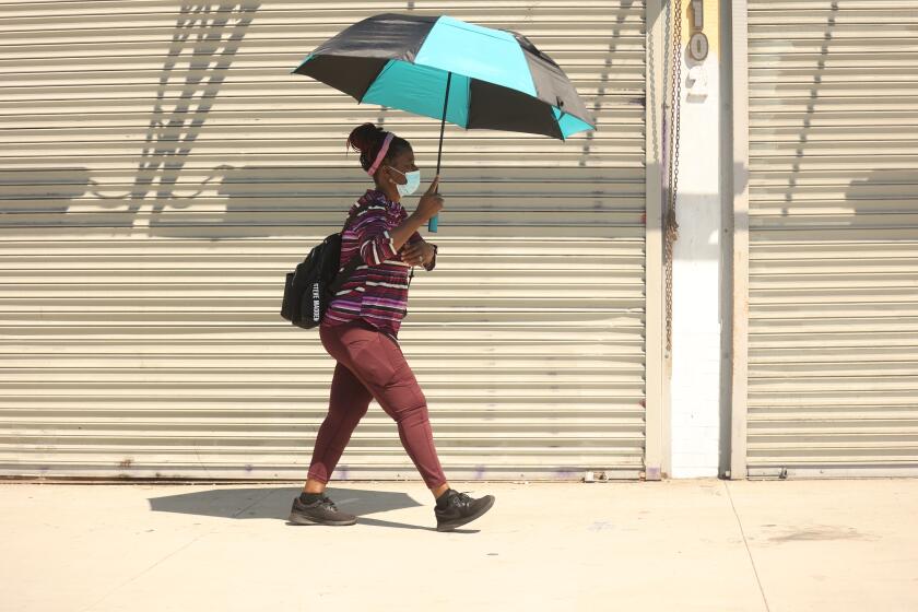 Leimert Park, CA - September 03: A woman walks with her unbrella to protect herself from the sun during a warm temperature day on Tuesday, Sept. 3, 2024 in Leimert Park, CA. (Michael Blackshire / Los Angeles Times)