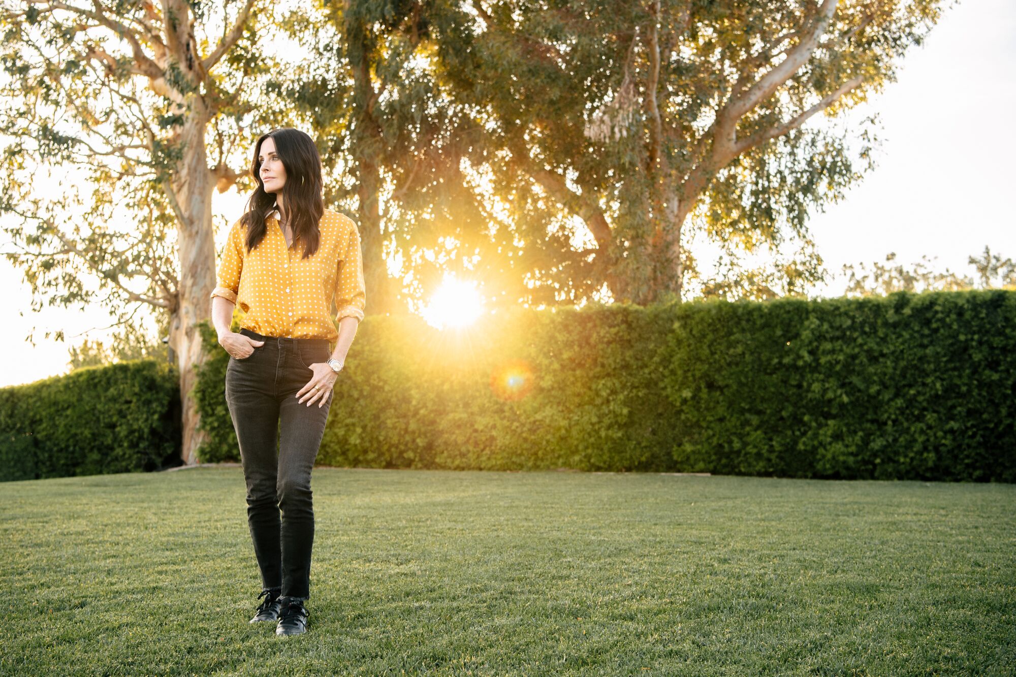 A woman in a button-down shirt and black jeans stands in a green yard.