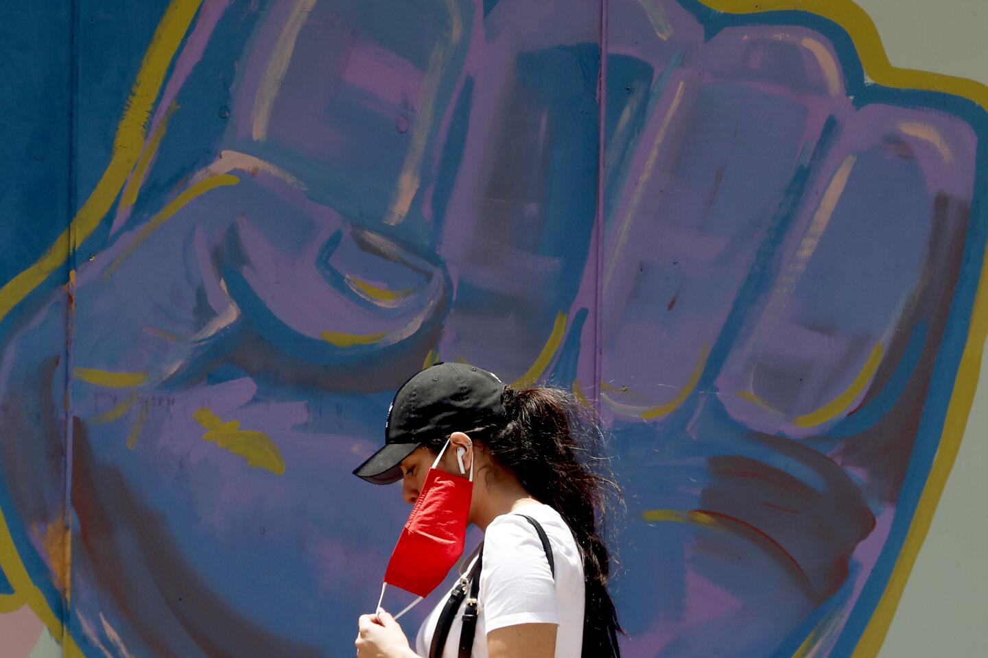 A woman adjusts a protective mask while walkiing along Atlantic Avenue in Long Beach.