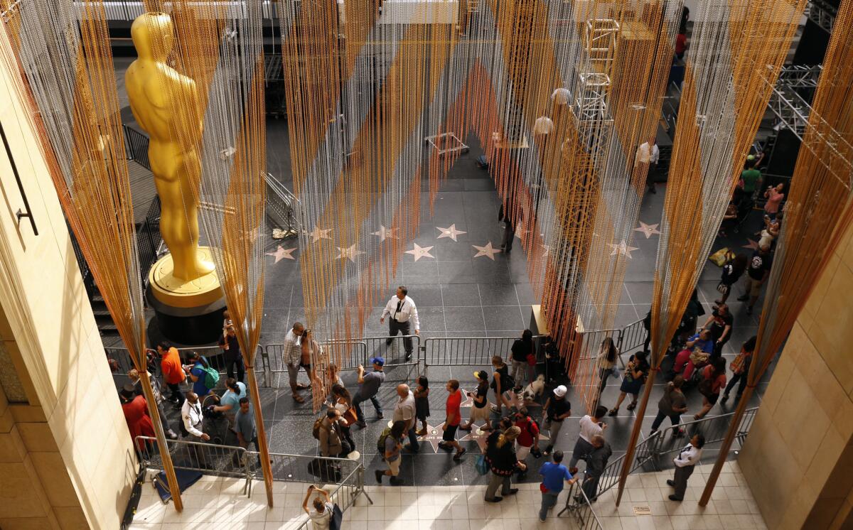 Pedestrians move past crews working on the Oscars' red carpet in front of the Dolby Theatre on Hollywood Boulevard.