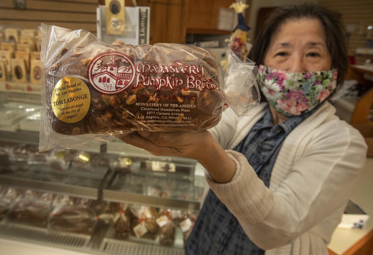 A woman in a mask holds a bag of pumpkin bread.