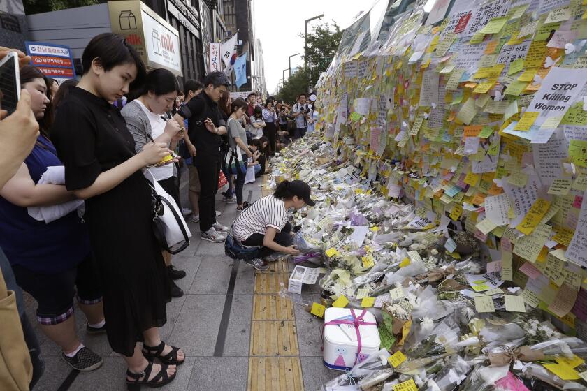 A woman places flowers for a South Korean woman who was stabbed to death at an exit of Gangham subway station in Seoul, South Korea, on Saturday, May 21.