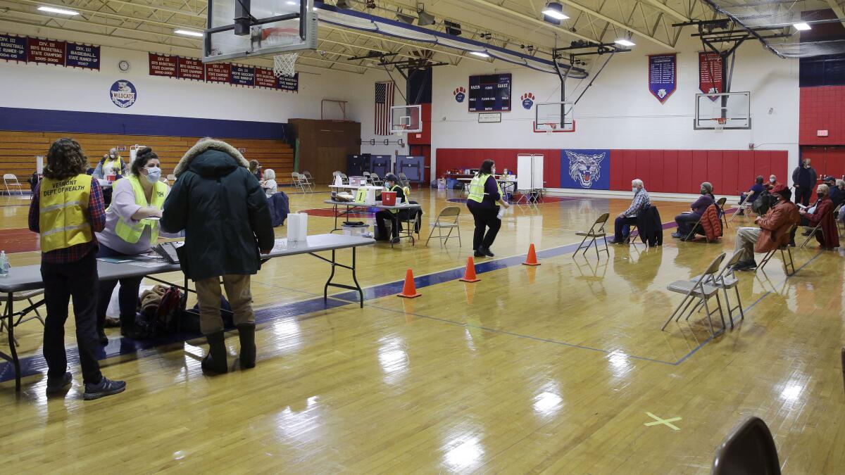 People wait for their turn to receive a COVID-19 vaccine at a high school gym.