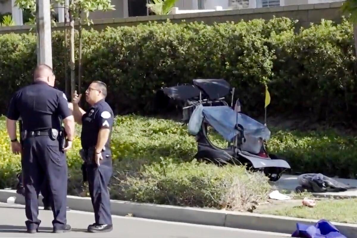 Two law enforcement officers talk near a jogging stroller that's on a sidewalk 