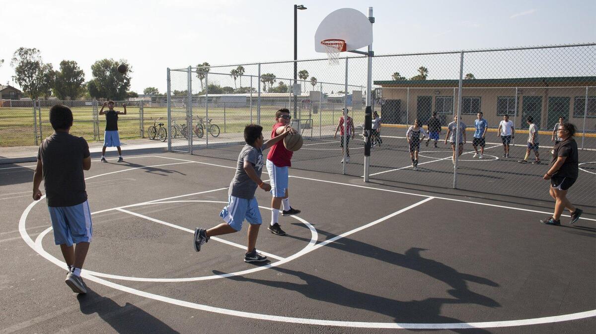 Students play around on the new basketball court and gated soccer area, background, at the new SOY, Save Our Youth, headquarters located behind Rea Elementary School in Costa Mesa on Wednesday.