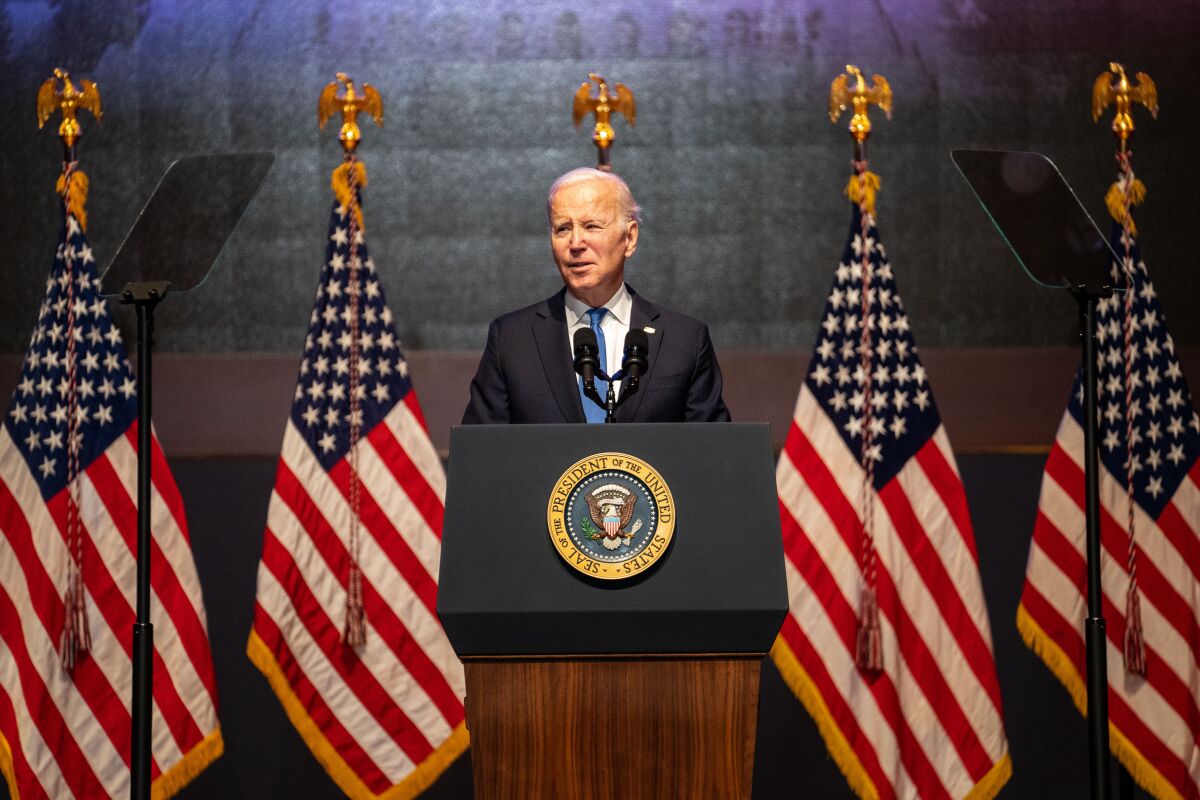 President Biden stands at a lectern with the presidential seal. U.S. flags are arrayed behind him. 