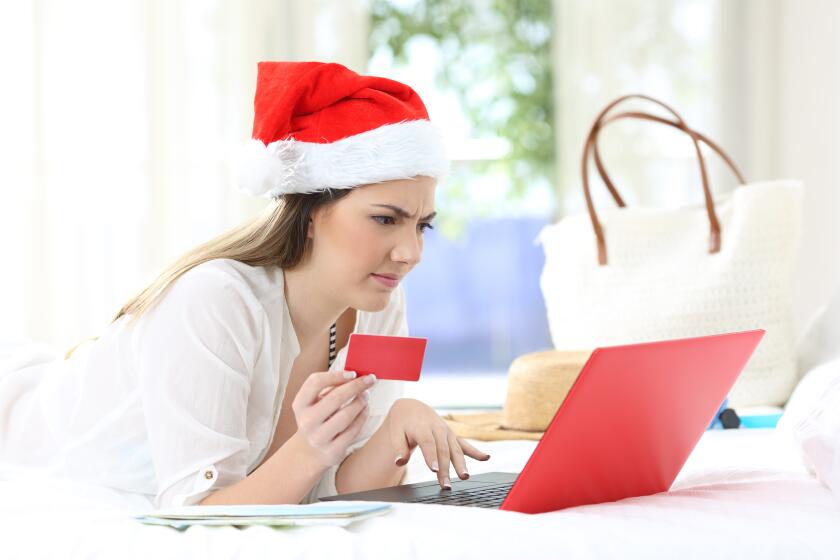 Confused woman paying online on christmas holidays lying on a bed in an hotel room