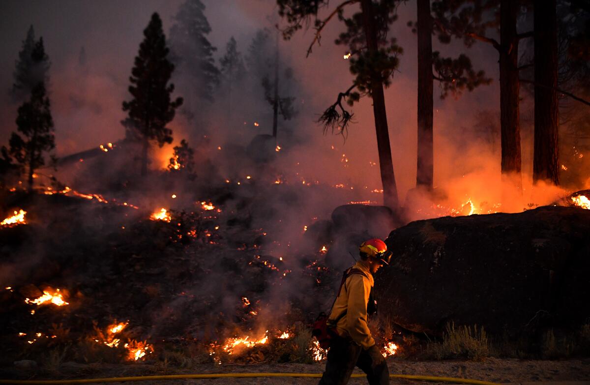 A firefighter at night walks through smoldering forestland illuminated by the glow of burning embers.