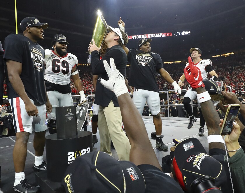Georgia head coach Kirby Smart kisses the trophy while Zamir White (from left) Jamaree Salyer, Nakobe Dean and quarterback Stetson Bennett celebrate on stage winning the College Football Playoff Championship game over Alabama, early Tuesday, Jan. 11, 2022, in Indianapolis. (Curtis Compton/Atlanta Journal-Constitution via AP)