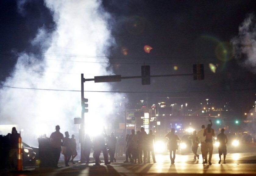 People stand near a cloud of tear gas during summer protests in Ferguson, Mo.