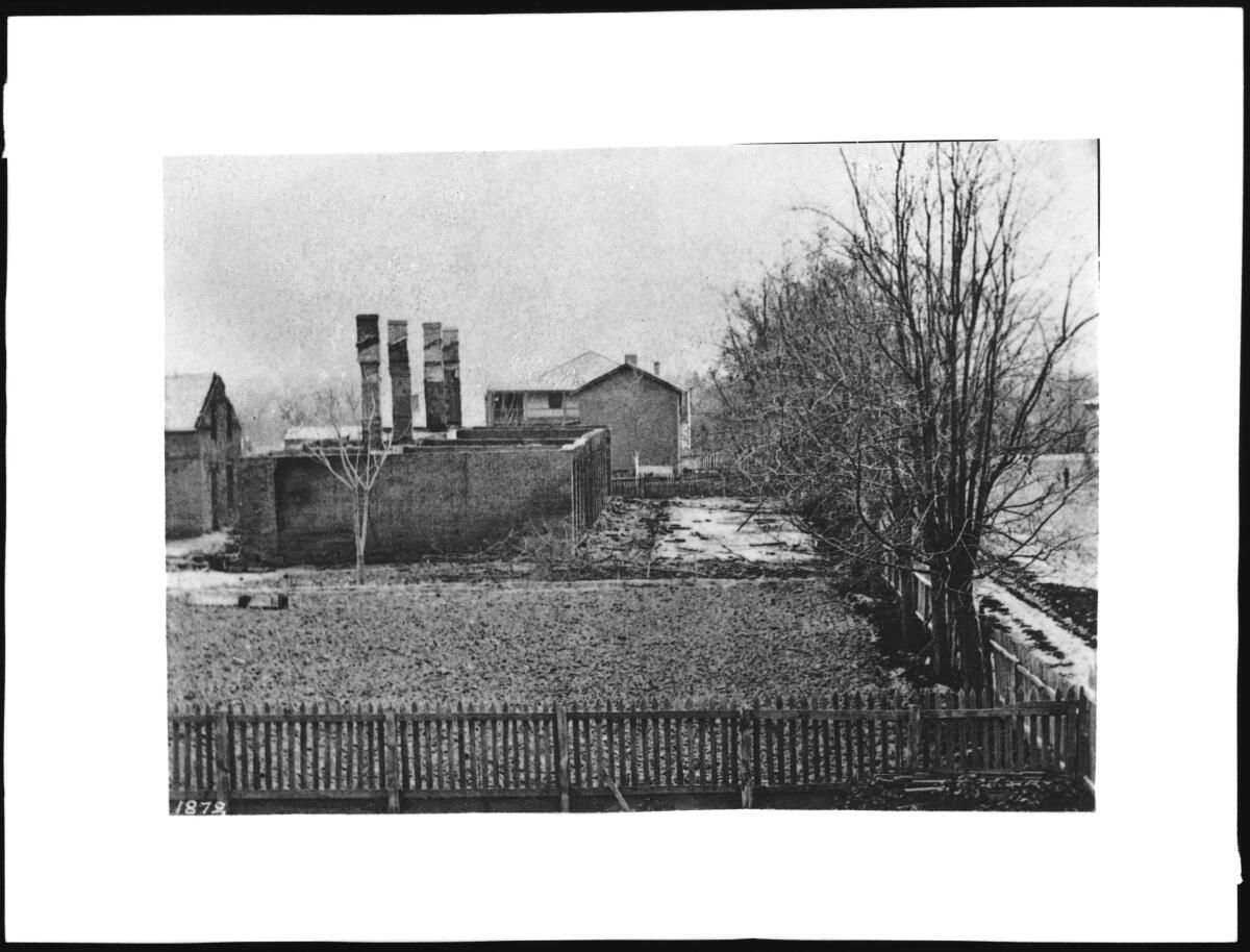 Black and white photo shows burned out buildings next to a stand of trees