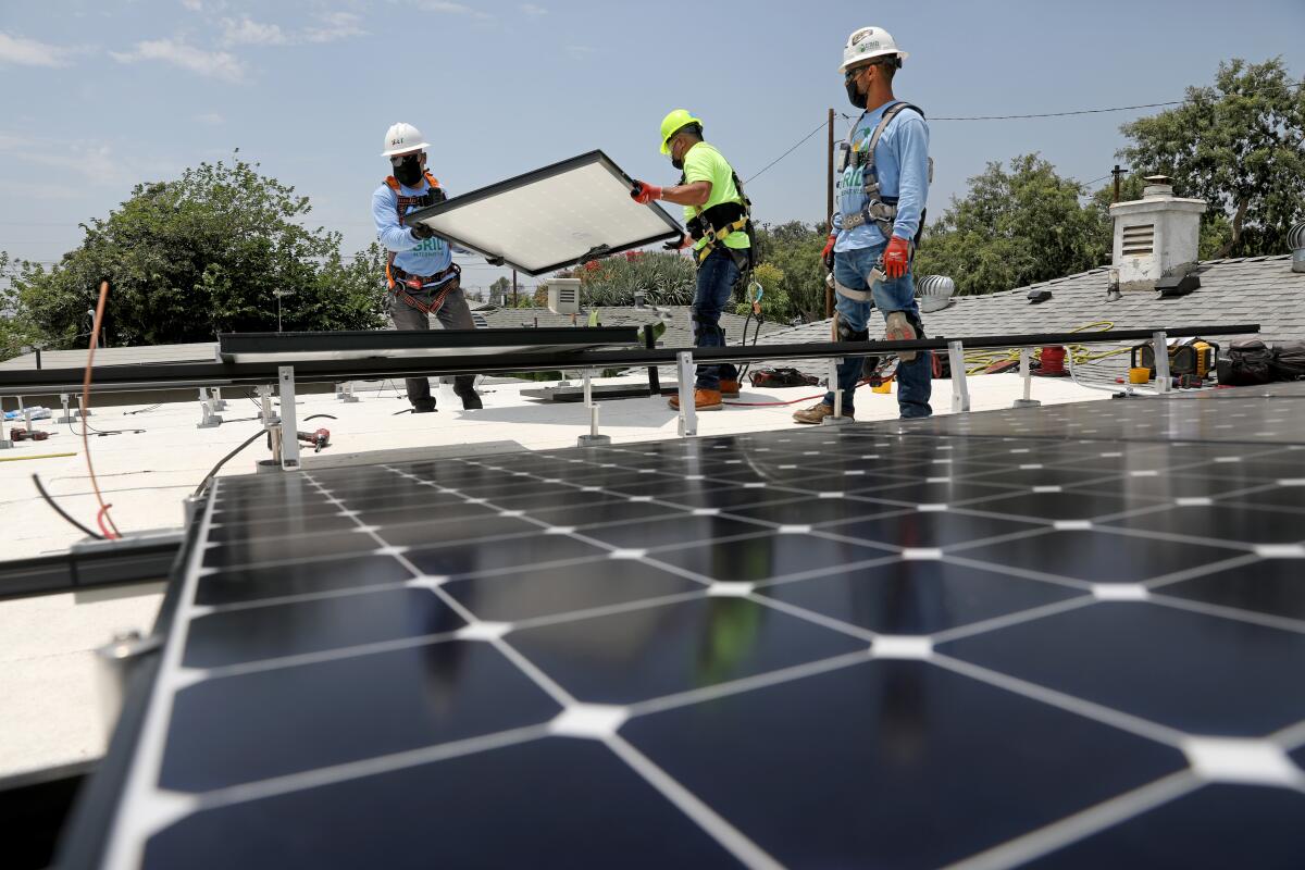 Employees of nonprofit solar installer GRID Alternatives place panels on the roof of a low-income home in Watts in 2021.