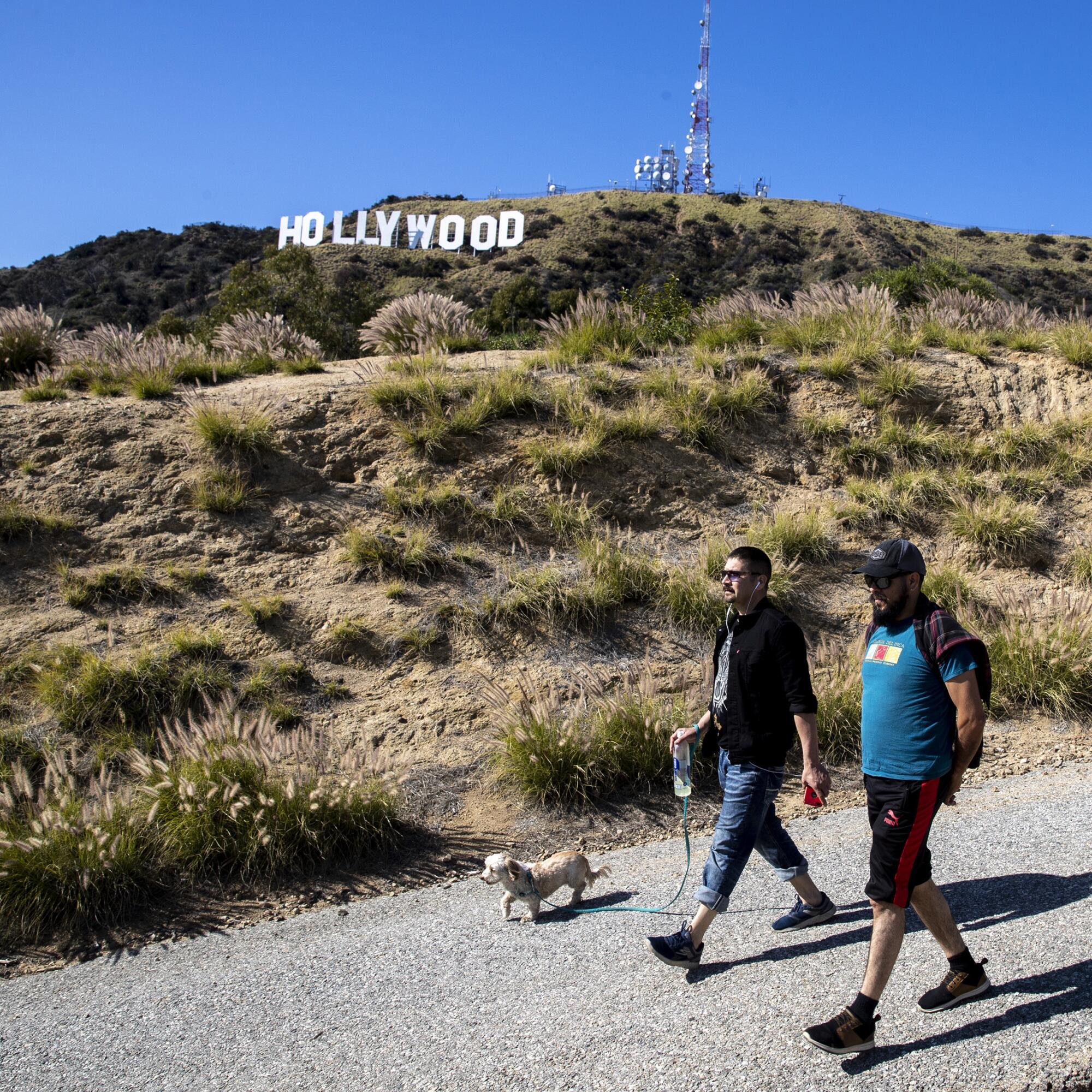 Hikers walk on a paved road in Griffith Park near the Hollywood sign.