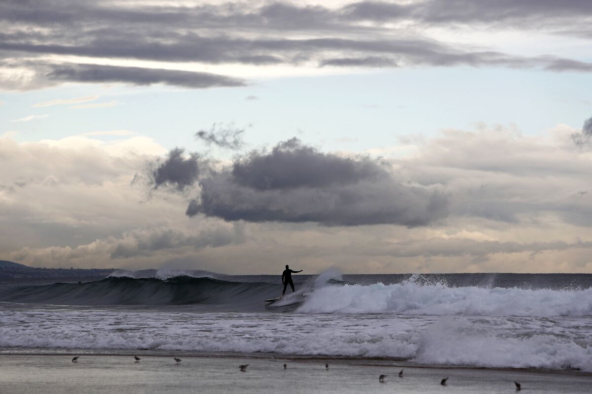 A surfer rides a wave near Newport Pier as clouds move inland on Wednesday evening in Newport Beach.