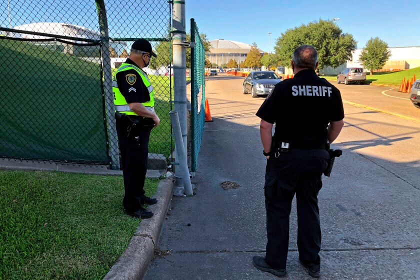HOUSTON, TX - OCT 31, 2020 - Harris County Sheriif's Deputy R. Hilz, right, and Houston Police Officer T. Jones (left) direct traffic Friday at a Houston stadium parking lot drive by polling place and drop site for mailed ballots. (Molly Hennessy-Fiske / Los Angeles Times)