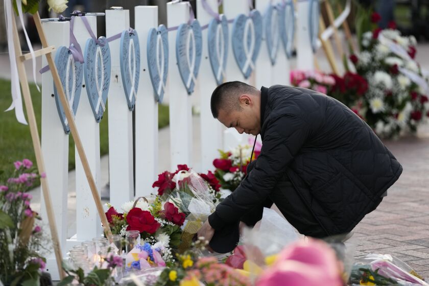 A man lays flowers near wooden hearts displaying names of victims at a vigil outside Monterey Park City Hall, blocks from the Star Ballroom Dance Studio on Tuesday, Jan. 24, 2023, in Monterey Park, Calif. A gunman killed multiple people at the ballroom dance studio late Saturday amid Lunar New Years celebrations in the predominantly Asian American community. (AP Photo/Ashley Landis)