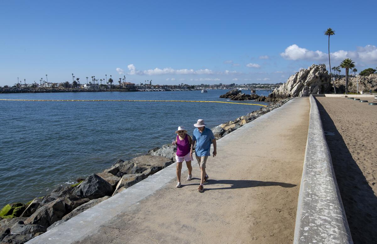 A couple walks along the jetty at Newport Harbor on Tuesday. A boom is stretched along the opening to the harbor. 
