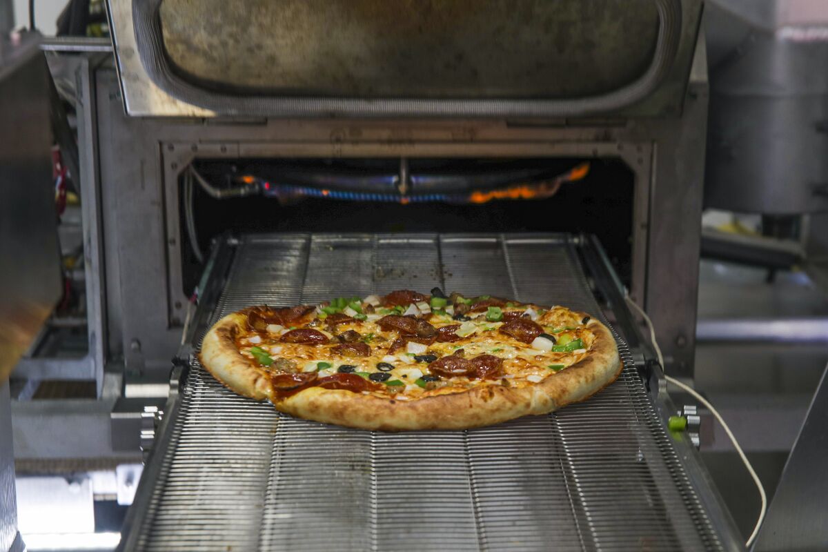 A finished pizza comes out of a deck oven.