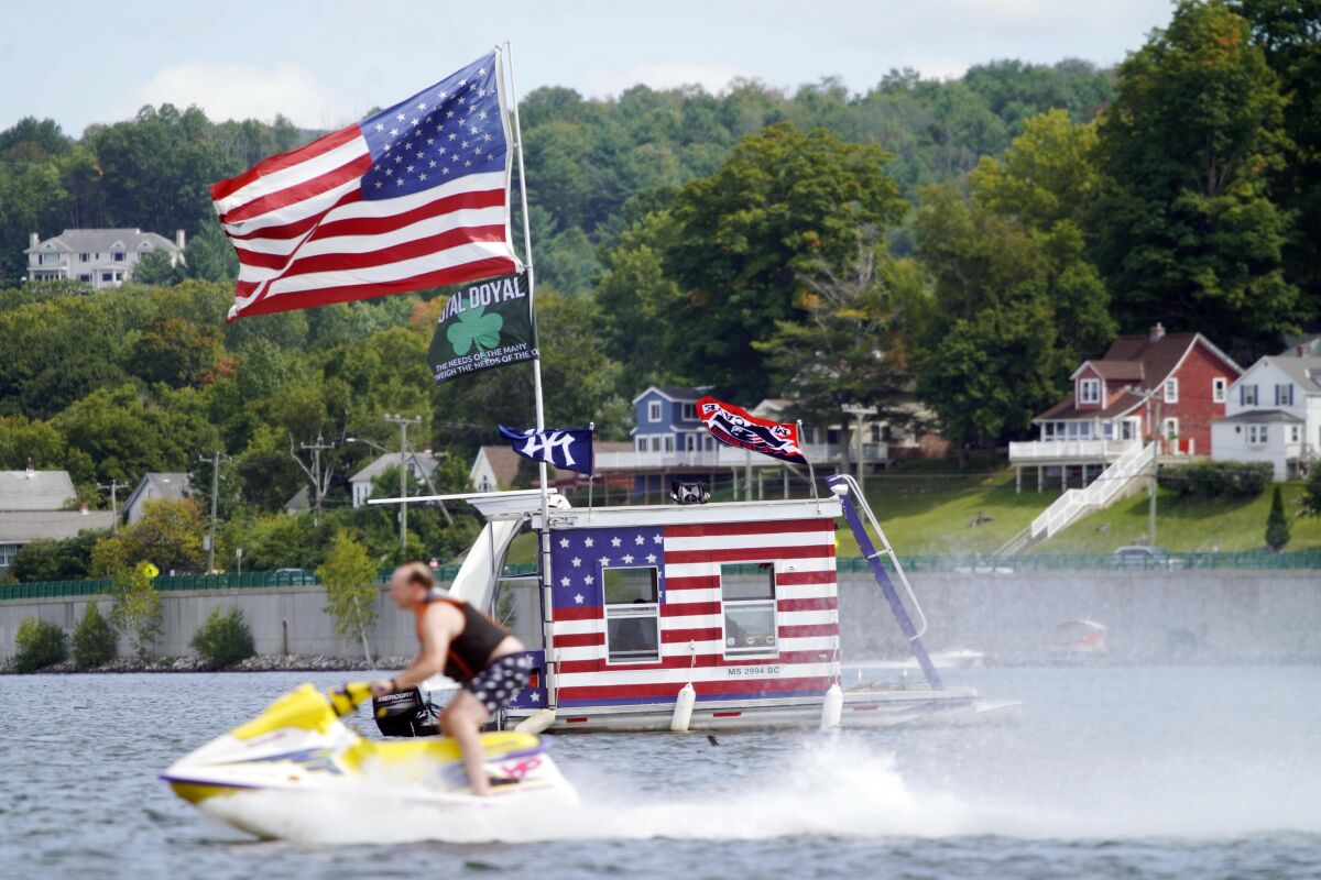 A jet skier passes a patriotic shanty-boat owned by AJ Crea on Pontoosuc Lake on Labor Day in Pittsfield, Mass., Monday, Sept. 7, 2020. (Ben Garver/The Berkshire Eagle via AP)